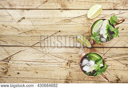 Moscow Mule Cocktails In Copper Mug With Lime, Ice, Ginger Beer, Vodka And Mint. Wooden Background, 