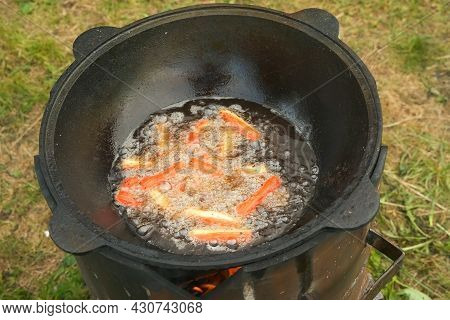 Frying Fish Sticks In Black Cazan With Boiling Oil In Wood-burning Stove On Nature. Many Ruddy Tasty