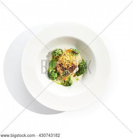 Panfried Fish with broccoli and cream sauce. Healthy roasted cod with green leaves. Fried Fish on white restaurant plate isolated on white background