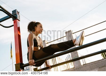 Concentarted young fit african fitness woman exercising on parallel bars at the sportsground