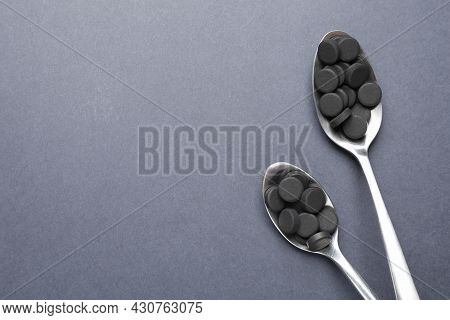Activated Charcoal Pills In Spoons On Grey Background, Flat Lay With Space For Text. Potent Sorbent