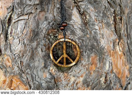 Close-up Of A Peace Sign Necklace Against A Tree Trunk Bark, Selective Focus