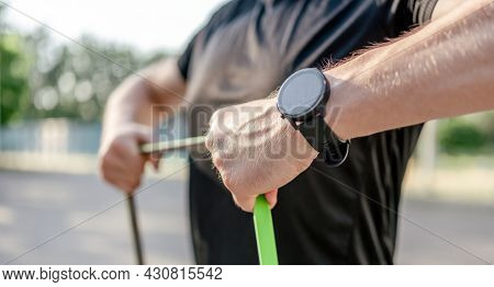 Sportive man guy training with elastic rubber band at the stadium outdoors with sunlight. Athlete male person during workout with additional sport equipmant