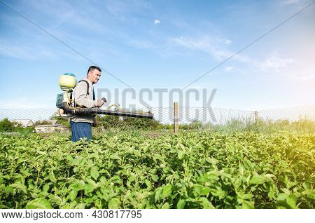 A Farmer With A Pesticide Sprayer Machine Walks Across The Field. Protection Of Plants From Insects 