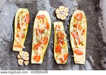 Raw Zucchini Halves, Ready To Bake, Stuffed With Cheese And Tomato On Baking Paper On A Baking Sheet