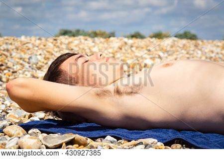 A 18 Year Old Caucasian Shirtless Teenage Boy Sunbathing On A Stoney Beach