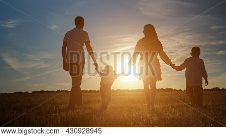 Family With Children Sons Silhouettes Walks Joining Hands Along Shadowed Field At Back Setting Sun I