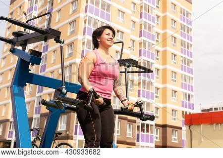 Young Woman Performing Bicep Curl Using Street Weight Machine In The City Yard