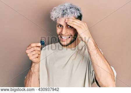 Young hispanic man with modern dyed hair holding sdxc card stressed and frustrated with hand on head, surprised and angry face 