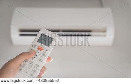 Hand Holding Remote Controller Directed On The Air Conditioner Inside The Room And Set At Ambient Te