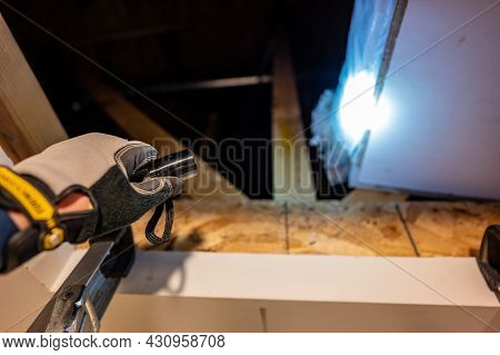 Shining A Hand Held Flashlight Into An Open Attic Entrance