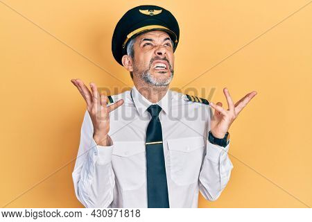 Handsome middle age man with grey hair wearing airplane pilot uniform celebrating mad and crazy for success with arms raised and closed eyes screaming excited. winner concept 