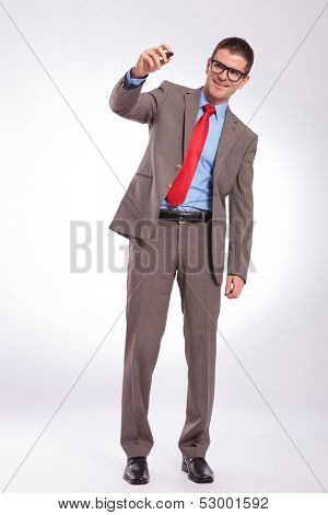 full length picture of a young business man writing on an imaginary screen with his marker while smiling. on a gray background