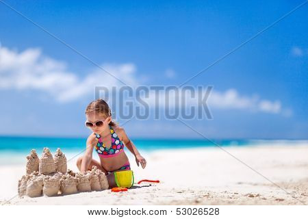 Little girl at tropical beach making sand castle