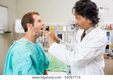 Side view of male doctor with depressor and otoscope checking patient's mouth in hospital