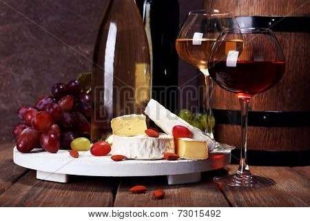 Supper consisting of Camembert cheese, wine and grapes on stand and wine barrel on wooden table on brown background