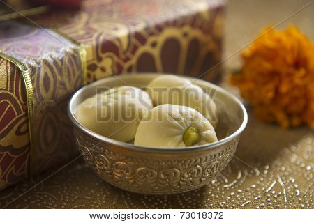 A bowl of an Indian sweet along with gift box in the background