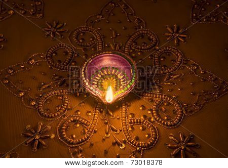 A traditional indian earthen lamp glowing on a golden luxurious embroidered background