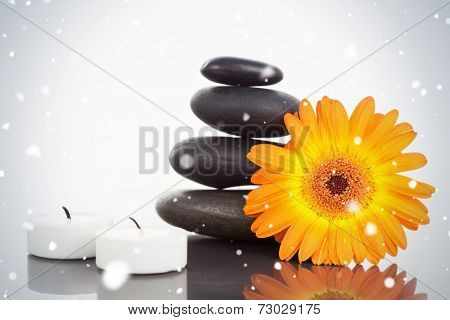 Composite image of snow falling against unlighted candles pebble stack an orange gerbera