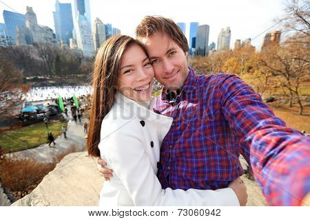 Dating young couple happy in love taking self-portrait selfie photo in Central Park, New York City in late fall early winter with skating rink in background. Tourists having fun date, Manhattan, USA.
