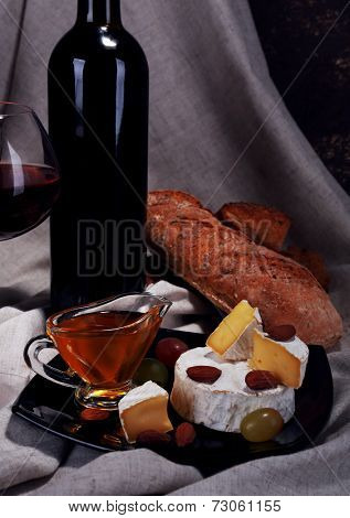 Supper consisting of Camembert and Brie cheese, honey, wine and grapes on napkin on curtain background