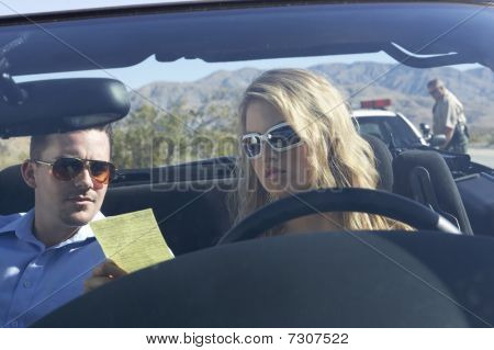 Casal sentado no carro olhando de multa de trânsito