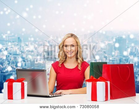 christmas, holidays, technology, advertising and people concept - smiling woman in red blank shirt with shopping bags, gifts and laptop computer over snowy city background