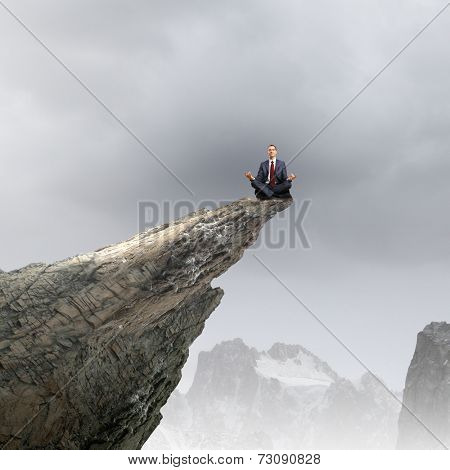Young businessman sitting lotus pose on edge of rock mountain