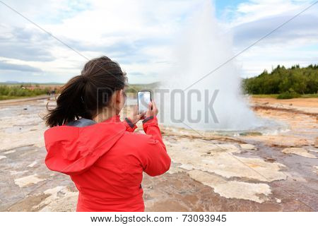 Iceland tourist taking photos of geyser Strokkur. Woman visiting famous tourist attractions and landmarks on the Golden Circle. Girl on holiday vacation sightseeing Icelandic nature.