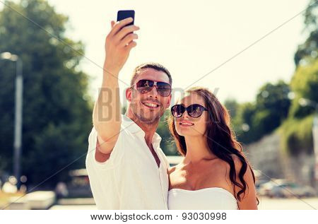 love, wedding, summer, dating and people concept - smiling couple wearing sunglasses making selfie with smartphone in park