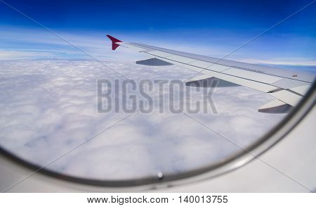 Wing of airplane flying above the clouds in the blue sky background through the window.