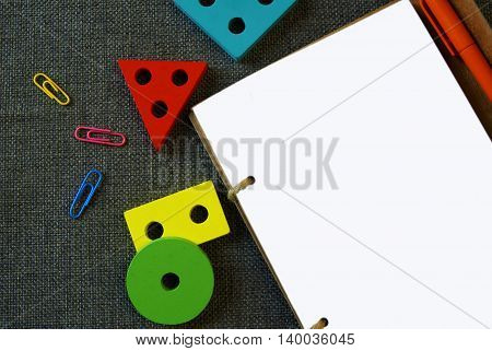Back to school. On textured fabric are notebook with a blank white page, next to him - clips and colored geometric shapes: circle, triangle, rectangle, square.