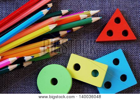 Back to school. Bright colored pencils and bright colored shapes (rectangle, circle, square, triangle) lie on a textured fabric on the table