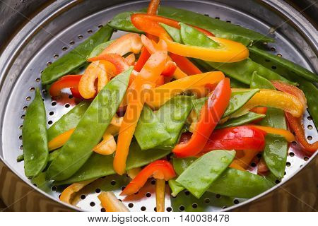 Bell pepper and snow pea stir-fry in stainless steel colander