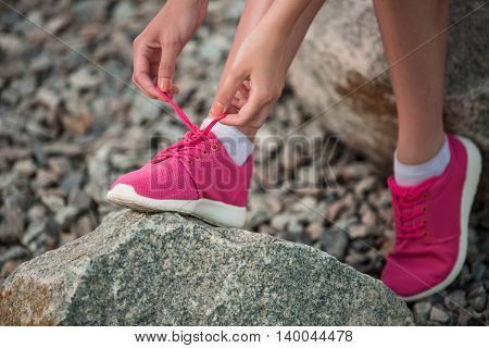 Running shoes - woman tying shoe laces. Closeup of female sport fitness runner getting ready for jogging outdoors on park path in late summer or fall.