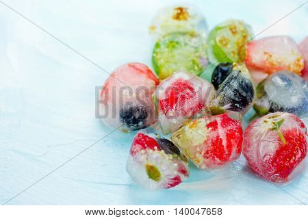 Fresh fruits and berry frozen in ice cubes on blue background. Fresh healthy summer cold eating blank space for text selective focus