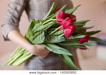 Closeup image of young woman with beautiful tulips. Young girl in a dress holding bunch of bright red spring flowers. Present for a woman.