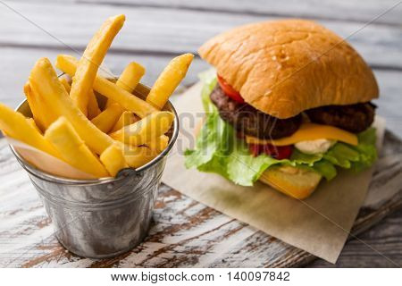Burger and bucket with fries. Fresh lettuce and bun. Typical fast food snack. Beefburger with cream cheese.