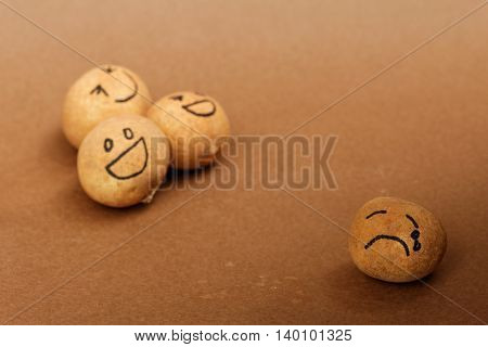 Group of brown ball laughing in the background while the brown ball in front alone,look sad and depressed.Different lighting and focusing to emphasize.Concept of discrimination,bully,mental illness.