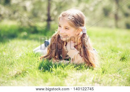 cute smiling little girl lying on the grass in park looking away