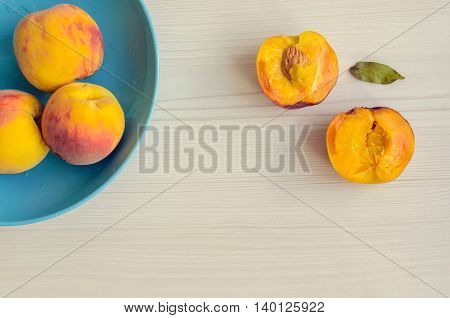 Ripe peaches in blue bowl on white wooden background. Group of fresh peaches on white table. Juicy and fresh peach with place for text. Concept for healthy eating and nutrition. Top view. Copy Space.