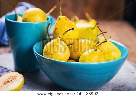 some raw ripe small yellow pears in blue dish on wooden background