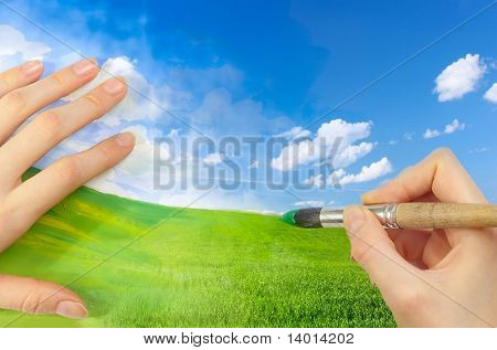 Mani con pennello disegno prato verde e blu cielo
