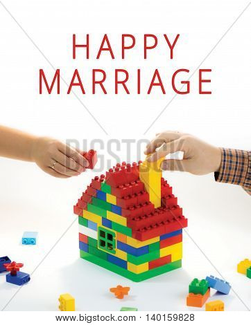 Toy house built by family - husband and wife. Their hands have rings. The symbol of building relationships