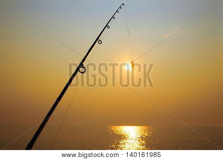 fly-fishing. fishing rod and jig on background of the setting sun. attempt to catch the setting sun fishing rod on the hook. the concept to extend the moment
