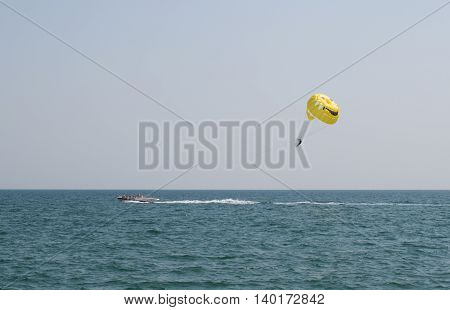 A man flying on a parachute behind the boat in the daytime