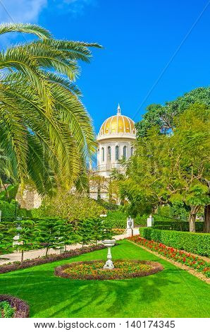 The Bahai Shrine surrounded by paradisiacal garden with shady palms trimmed bushes and colorful flower beds also decorated with small sculptures and fountains Haifa Israel.