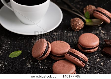 Chocolate french macarons with ganache filling on a black table with coffee