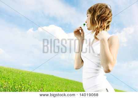 Young woman in white shirt with grass stem standing on green meadow