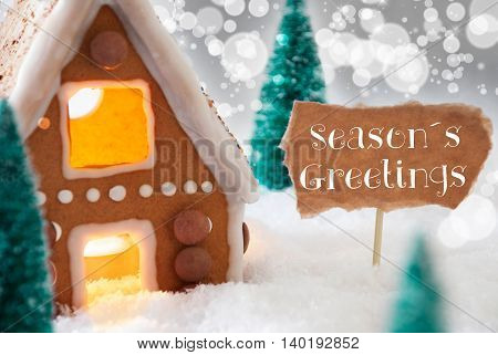 Gingerbread House In Snowy Scenery As Christmas Decoration. Christmas Trees And Candlelight For Romantic Atmosphere. Silver Background With Bokeh Effect. English Text Seasons Greetings